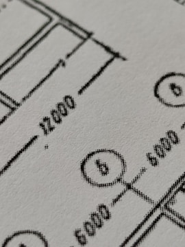 Close-up view of a technical drawing or blueprint featuring measurements and diagrams. The image shows lines, numbers, and symbols commonly used in architectural or engineering designs.