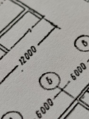 Close-up view of a technical drawing or blueprint featuring measurements and diagrams. The image shows lines, numbers, and symbols commonly used in architectural or engineering designs.