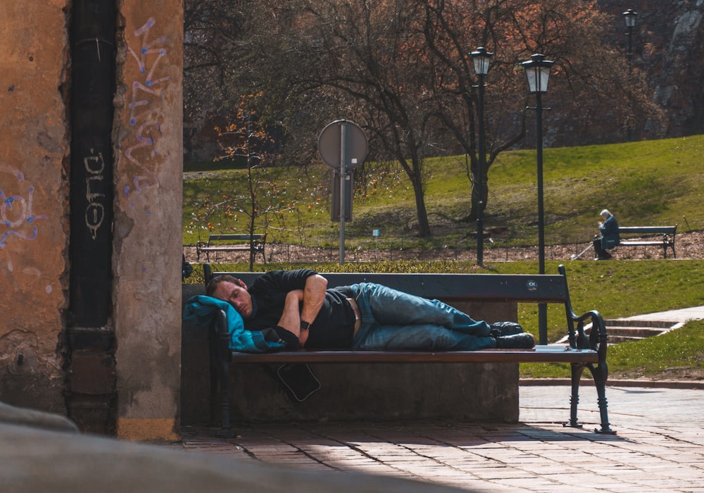 man in blue shirt lying on black bench