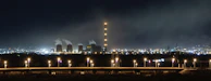 Night shot of a petrochemical complex illuminated with bright lights and steam rising.