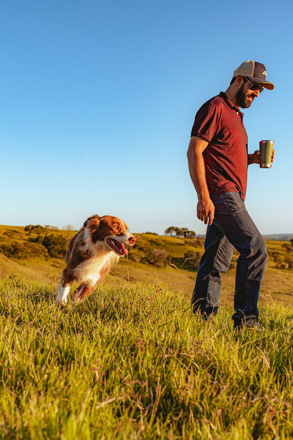 man in brown polo shirt and blue denim jeans holding brown and black dog