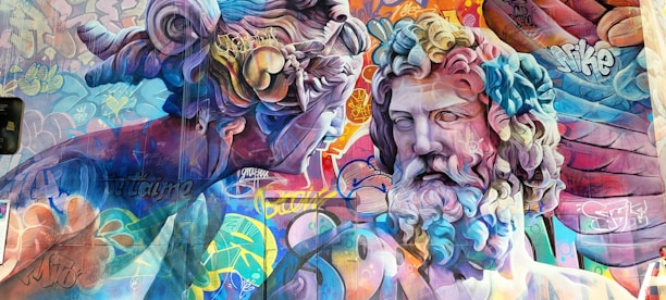 A vibrant mural featuring two classical-style sculptures interwoven with colorful graffiti art. The sculptures have intricate details with swirling hair and expressive faces, surrounded by layers of vivid graffiti text and patterns. The use of bright and bold colors enhances the dynamic contrast between the traditional sculptures and modern street art elements.