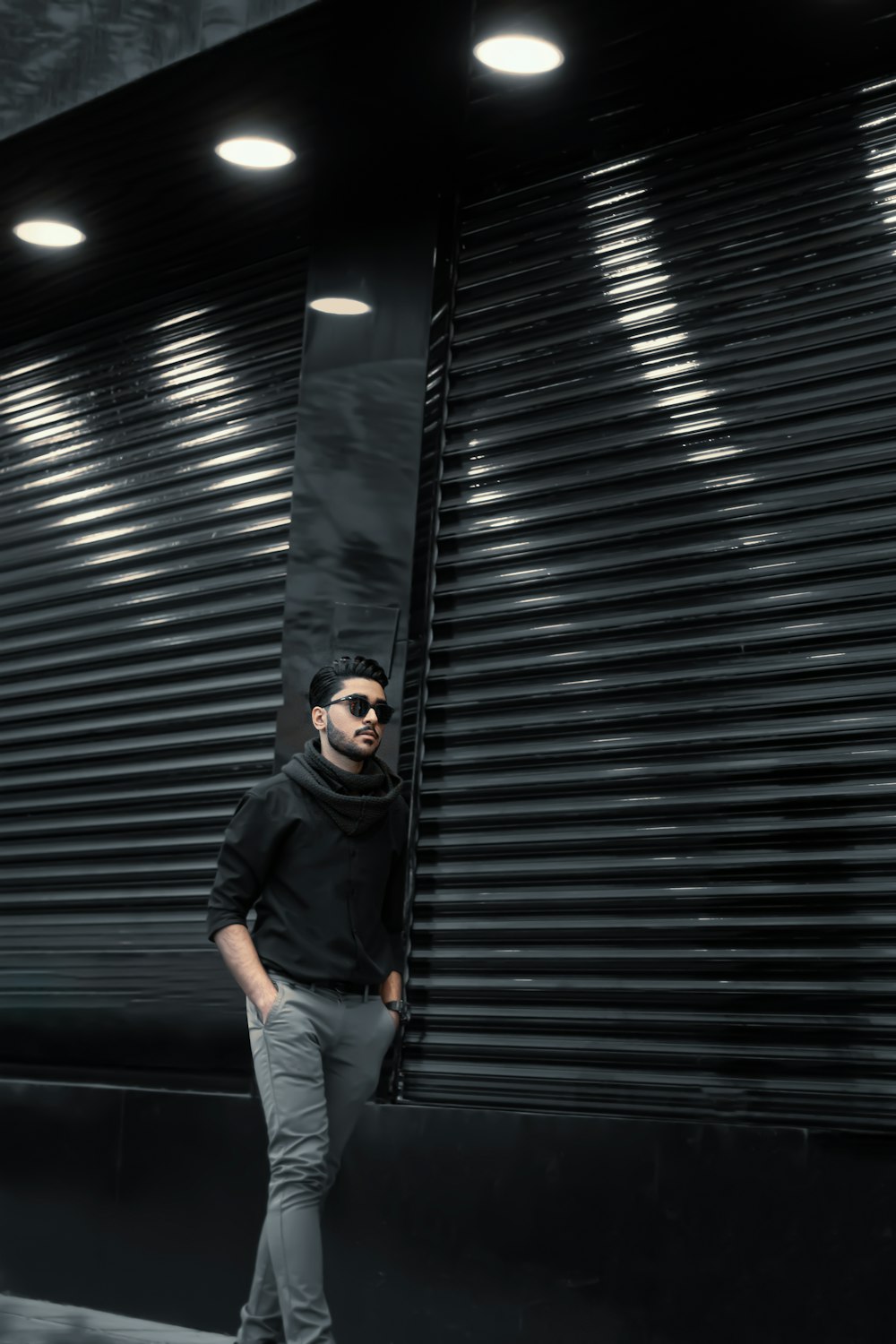 man in black jacket and blue denim jeans standing beside roll up door