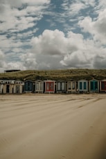 red and white wooden house on brown sand under white clouds during daytime