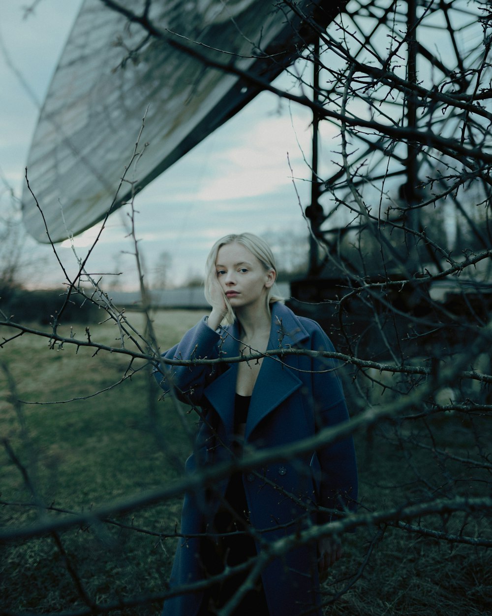 woman in blue coat standing near bare trees during daytime