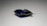 A close-up of a single laundry detergent pod with a combination of dark blue and clear gel segments, packaged in a transparent plastic wrapper. The background is a neutral gray, contrasting with the vivid colors of the pod.