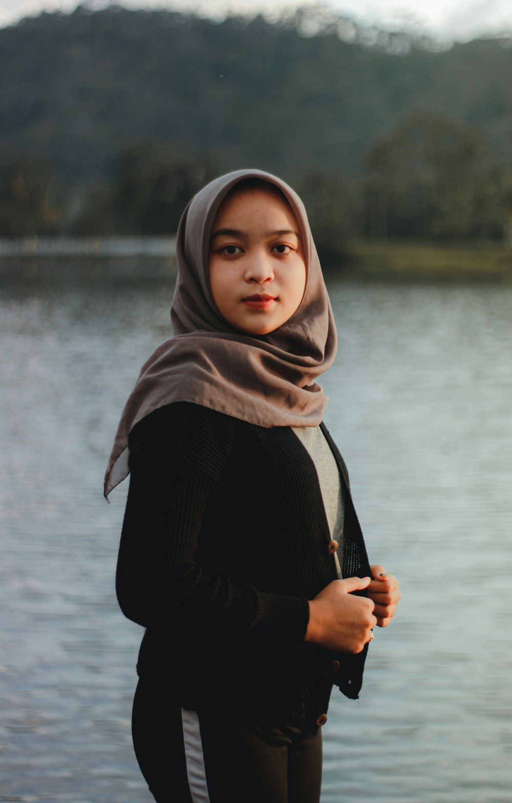 woman in brown hijab and black long sleeve shirt standing near body of water during daytime
