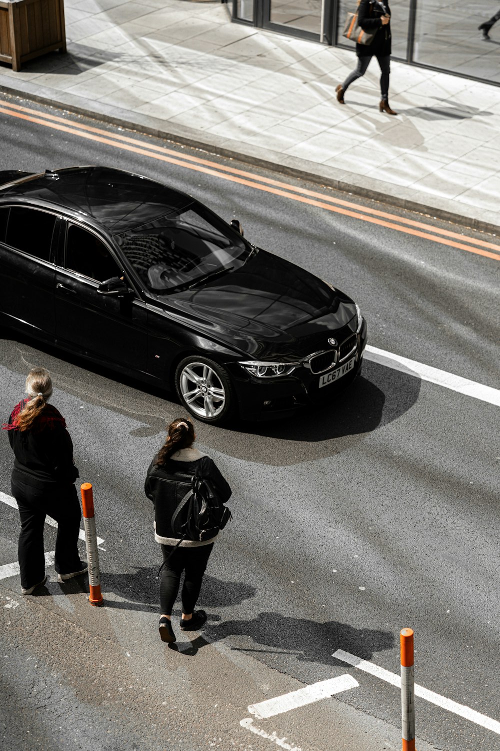 man in black jacket standing beside black bmw m 3