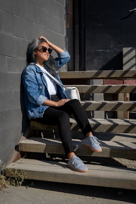 woman in blue jacket and black pants sitting on brown wooden bench