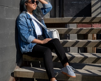 woman in blue jacket and black pants sitting on brown wooden bench