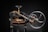 A vintage mechanical device composed of mainly black metal with some brass elements. The machine features a large hand wheel, connected via rods and levers, and includes a cutting blade at the base. Intricate components and gears add to the complexity of the machinery.