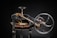 A vintage mechanical device composed of mainly black metal with some brass elements. The machine features a large hand wheel, connected via rods and levers, and includes a cutting blade at the base. Intricate components and gears add to the complexity of the machinery.