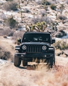 A rugged SUV on a desert trail with red rocks and cacti in the background.