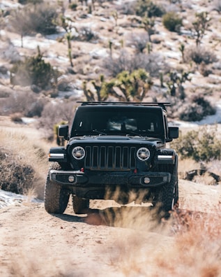 A rugged SUV on a desert trail with red rocks and cacti in the background.