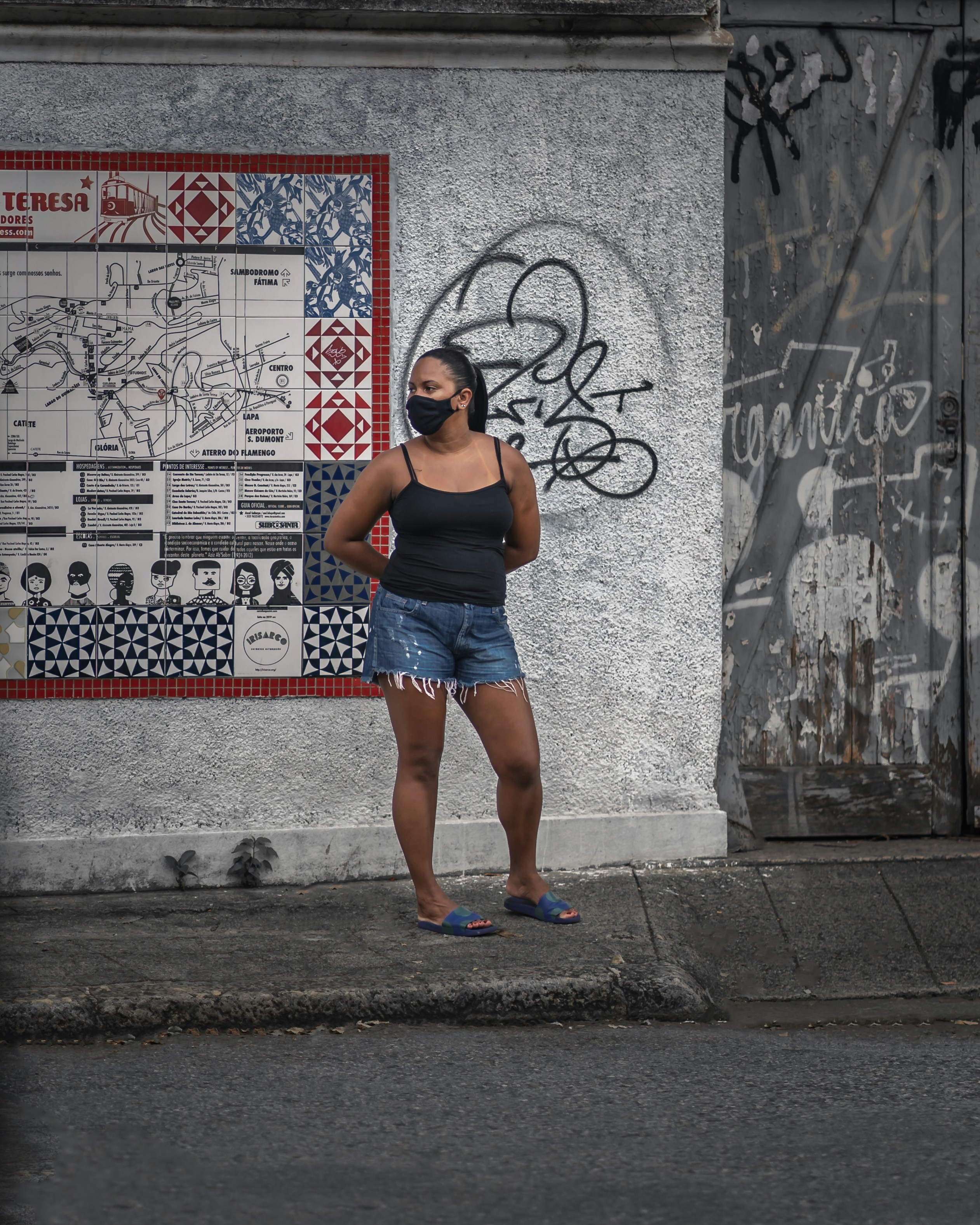 woman in black tank top and blue denim shorts standing on sidewalk during daytime