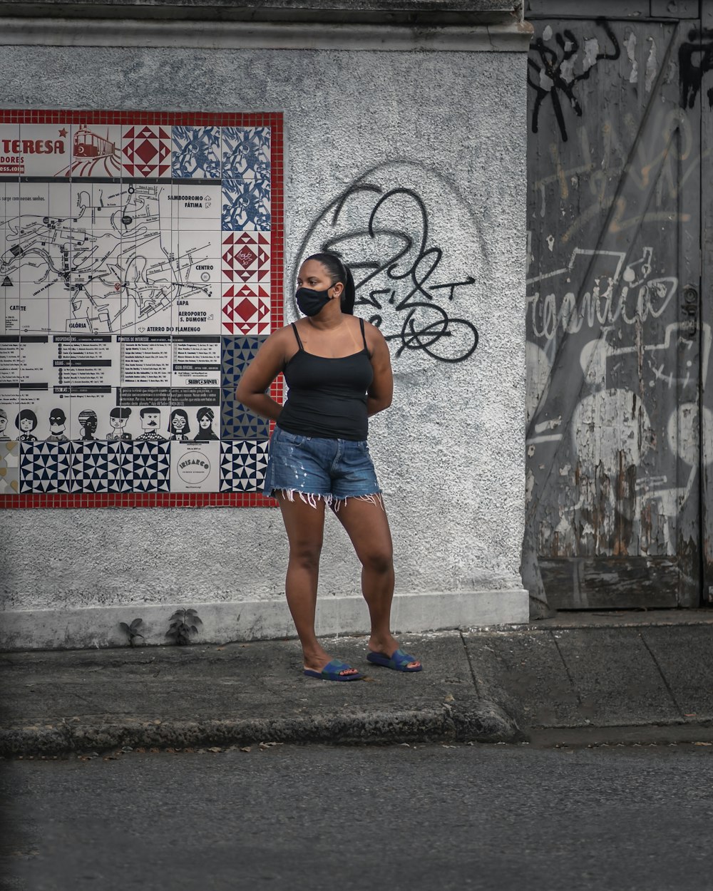 woman in black tank top and blue denim shorts standing on sidewalk during daytime