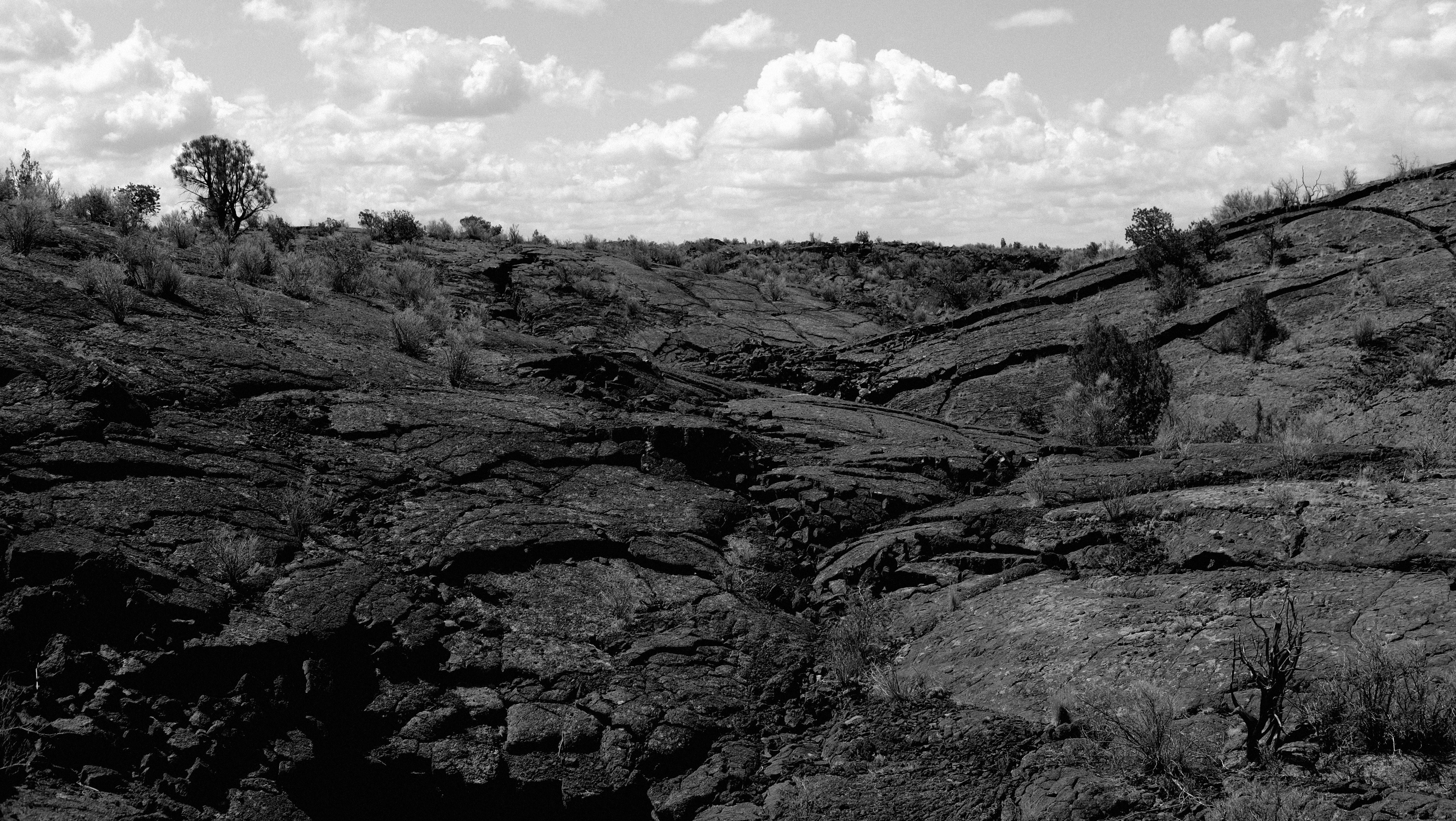 grayscale photo of rocky mountain under cloudy sky