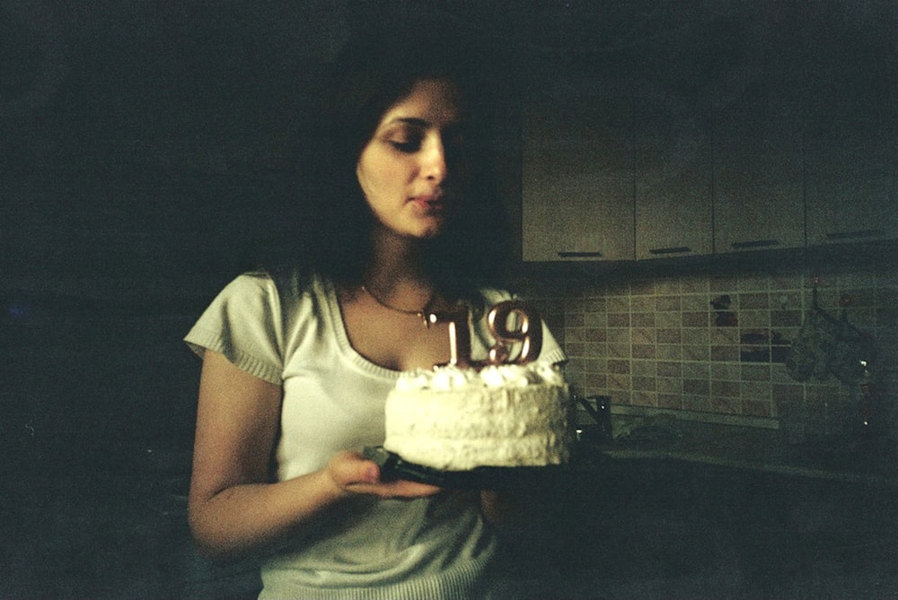 woman in white scoop neck t-shirt holding cake