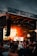 A vibrant music festival scene with a large stage, featuring a performer silhouetted against a backdrop of fiery orange lights. The audience is gathered, enjoying the energetic atmosphere while waving their hands. A large beach ball is visible bouncing among the crowd.