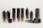 A collection of sleek lip cream containers in various shades, arranged neatly. Some tubes are open showing the applicators.