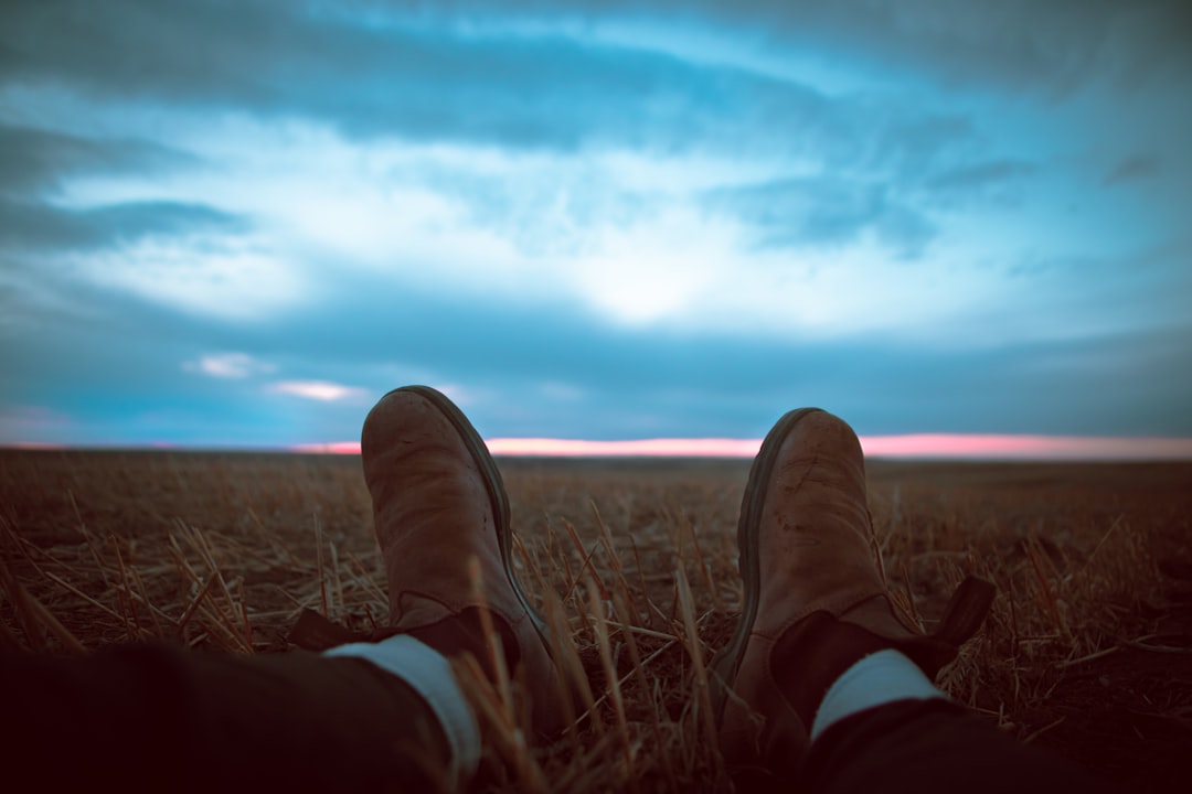 person in brown leather boots sitting on brown grass field during daytime