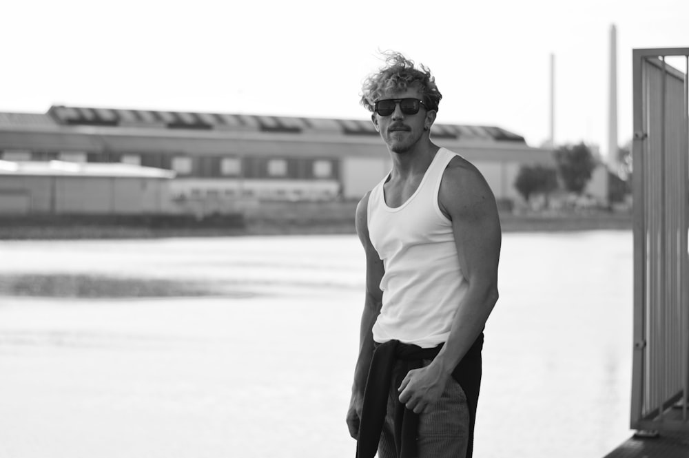 man in white tank top and black pants wearing sunglasses standing on white sand during daytime