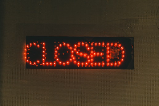 A rectangular black sign displays the word 'CLOSED' in bright red LED lights. The lights stand out against the dark background, creating a clear and attention-grabbing message. The dots formed by the LED lights give the text a digital appearance.