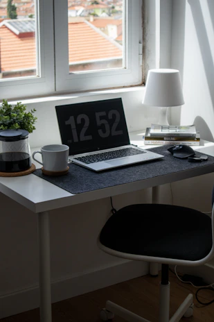 A clean, minimalist workspace with a laptop, notebook, and coffee cup bathed in natural light.