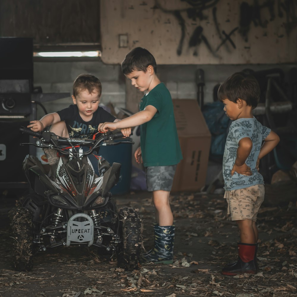 man in green t-shirt standing beside boy in blue t-shirt riding on black motorcycle