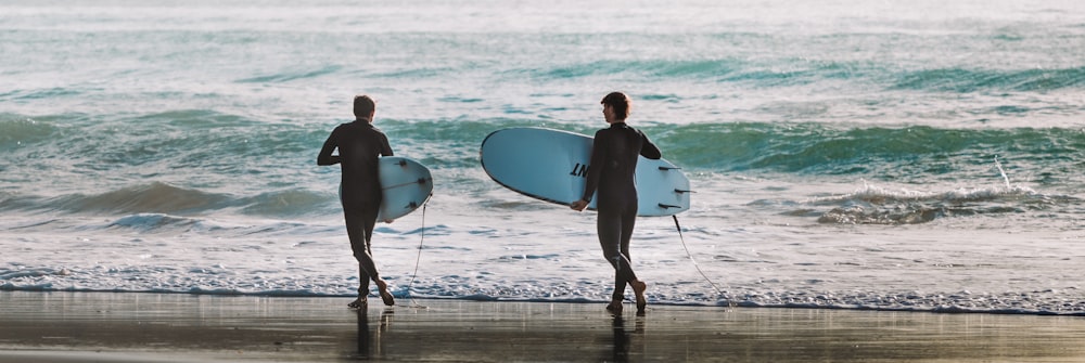 낮 동안 해변에서 흰색 서핑 보드를 들고 걷는 남자와 여자