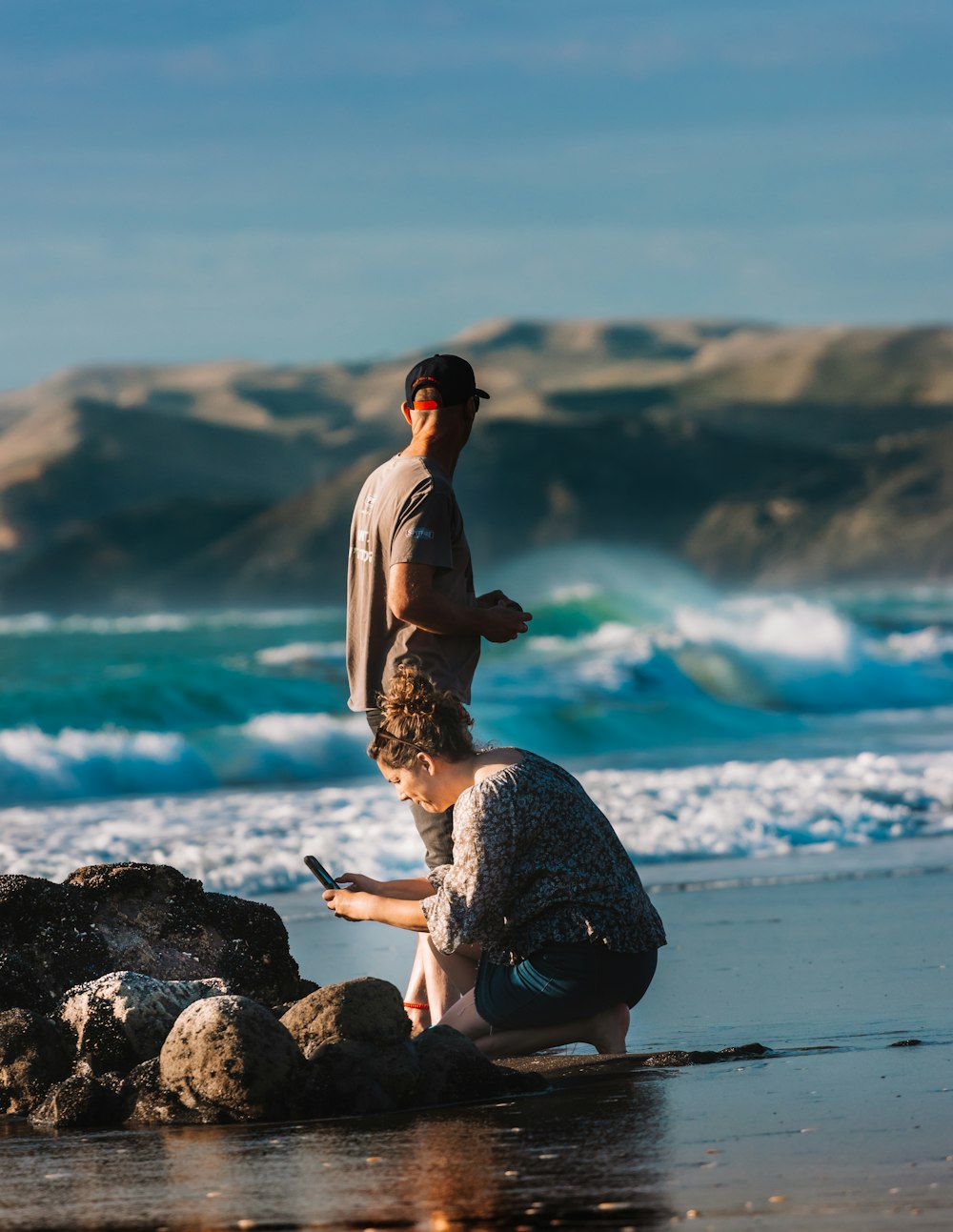 hombre y mujer sentados en la roca cerca del mar durante el día
