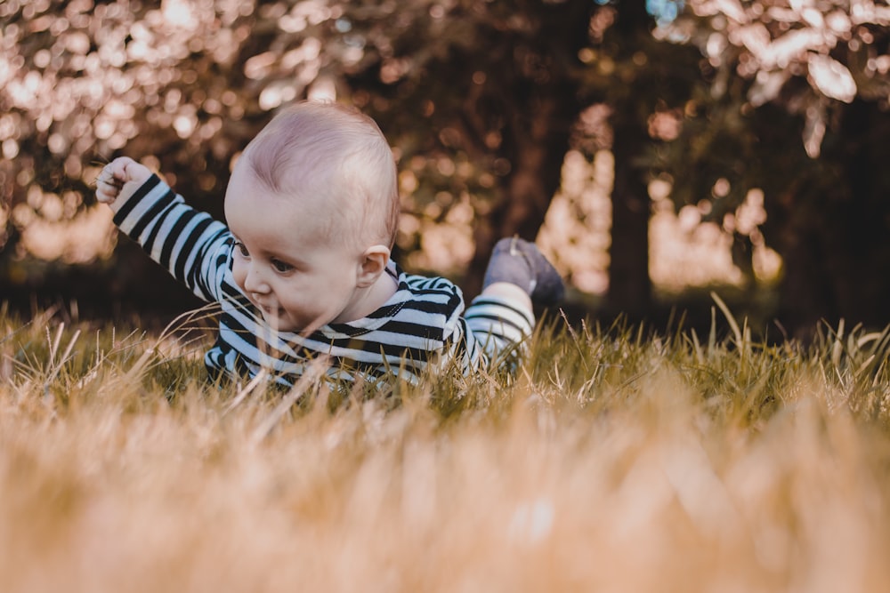 baby in blue and white striped onesie lying on green grass during daytime