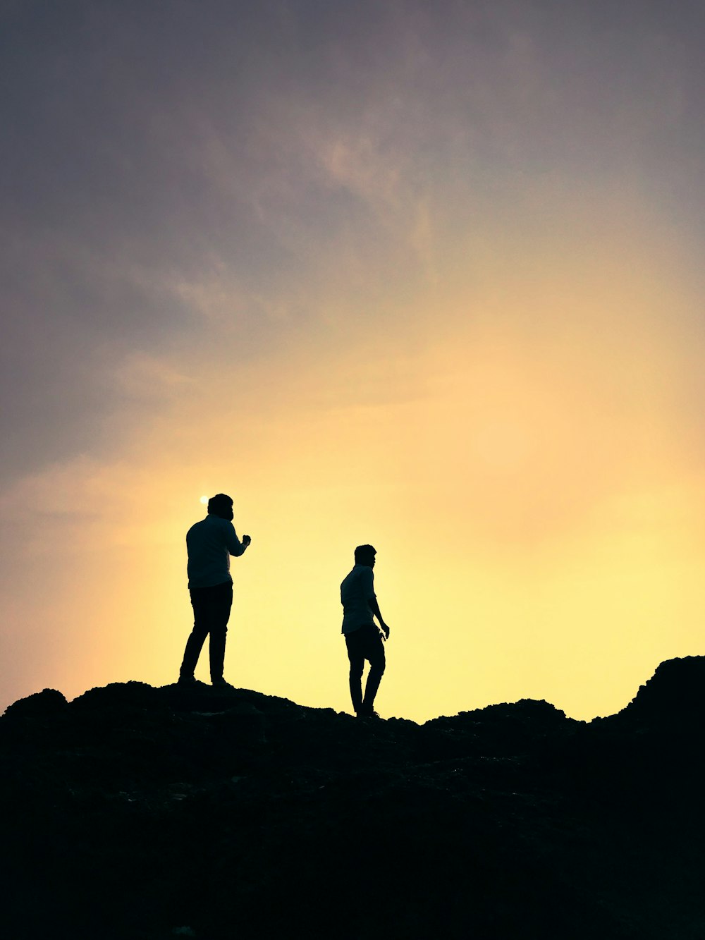 silhouette of 2 men standing on rock formation during sunset