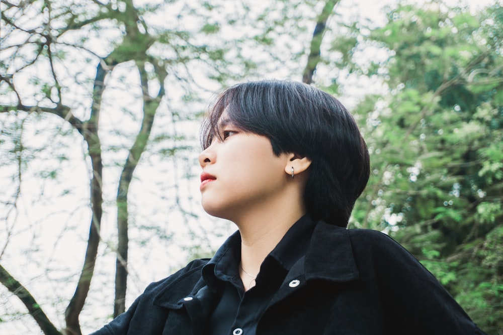 woman in black leather jacket standing under green tree during daytime