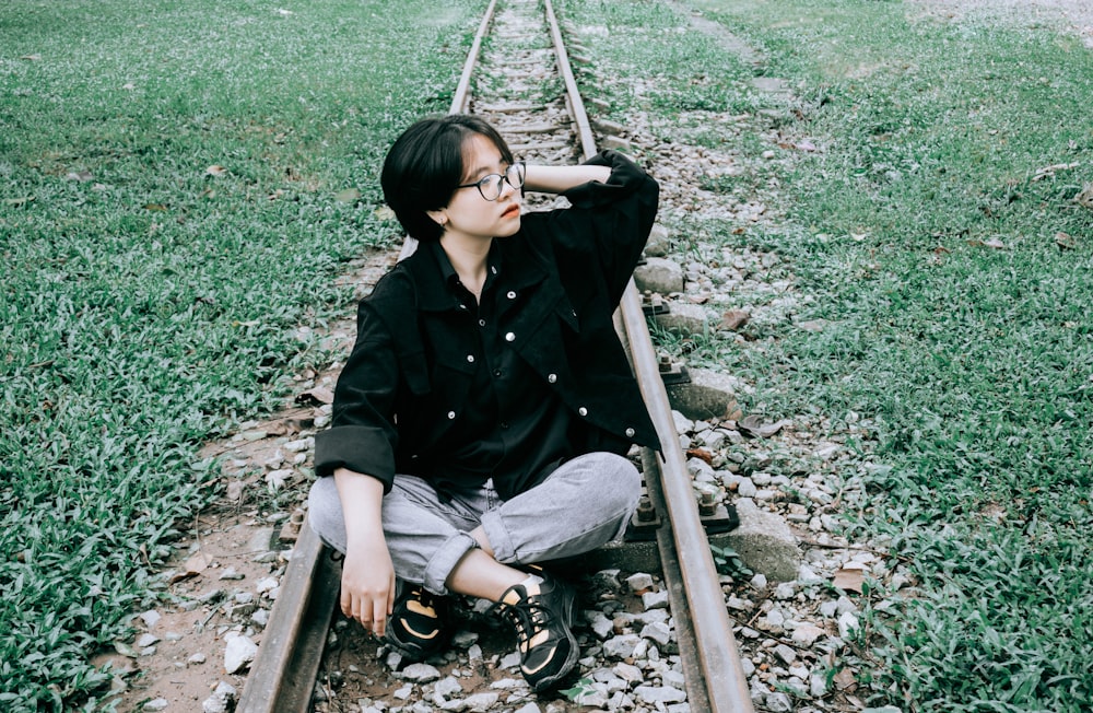 Frau in schwarzer Jacke sitzt tagsüber auf der Bahnschiene