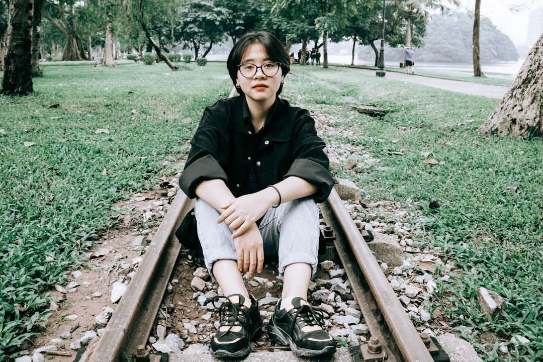 woman in black jacket sitting on brown wooden bench, Teenager girl posing at the railway