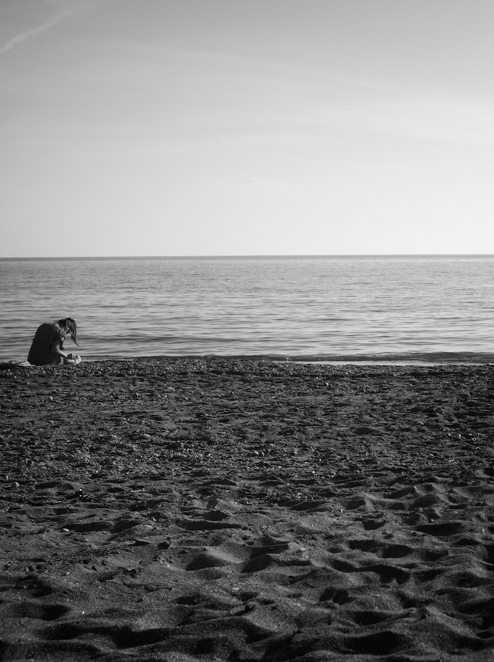 Foto in scala di grigi della donna che si siede sulla spiaggia