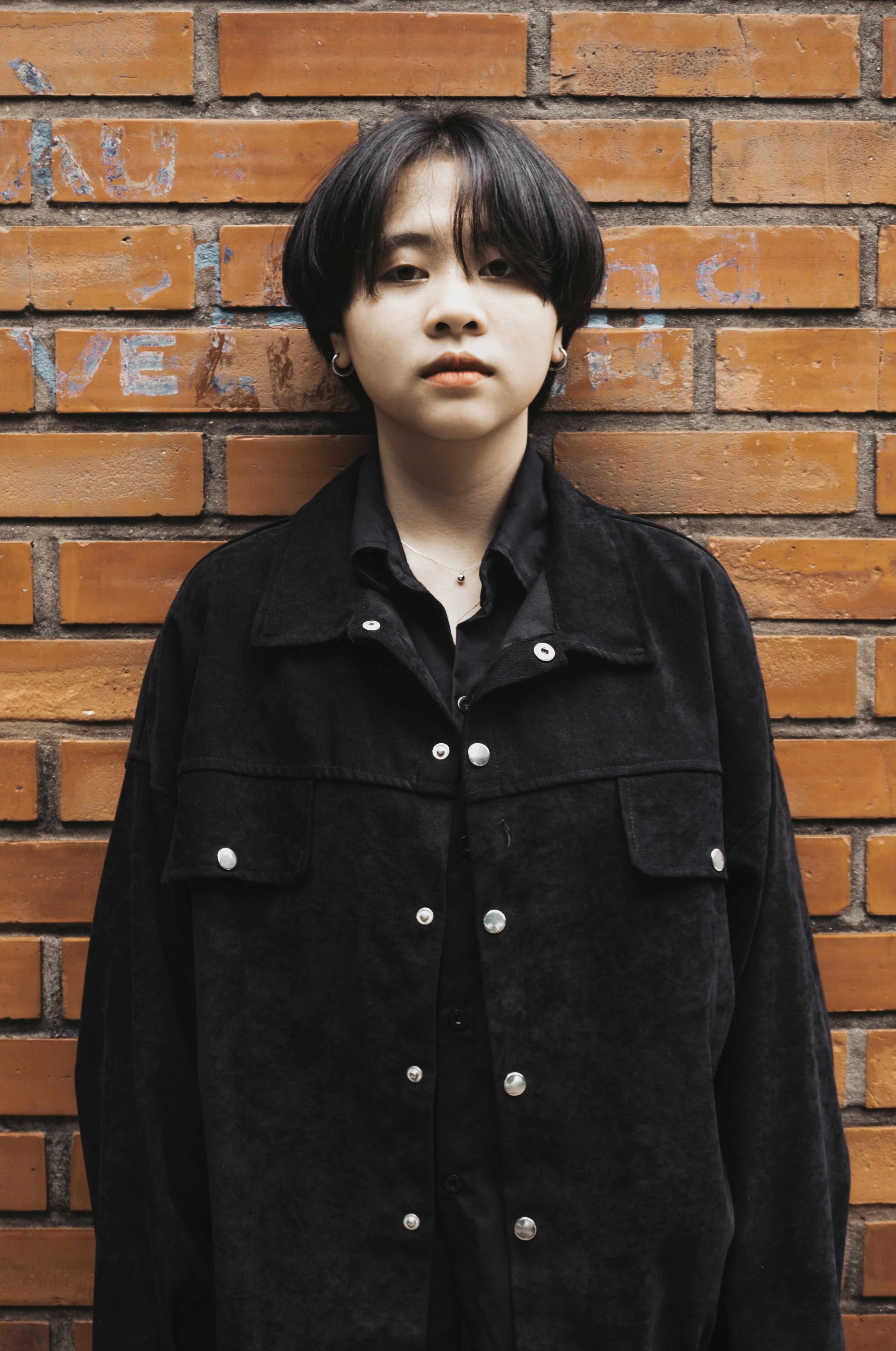 woman in black button up coat standing beside brown brick wall