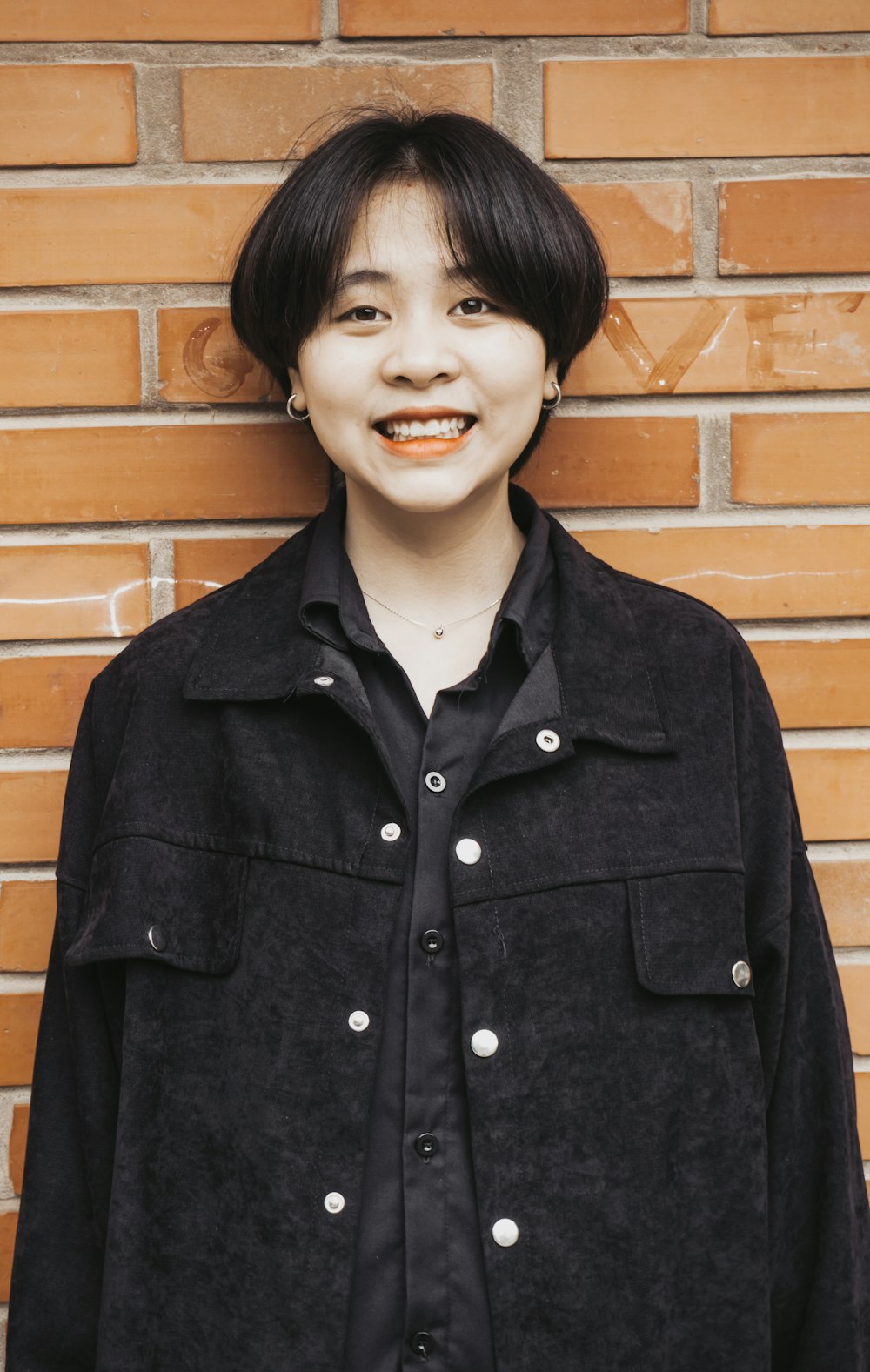 woman in black button up shirt standing beside brown brick wall