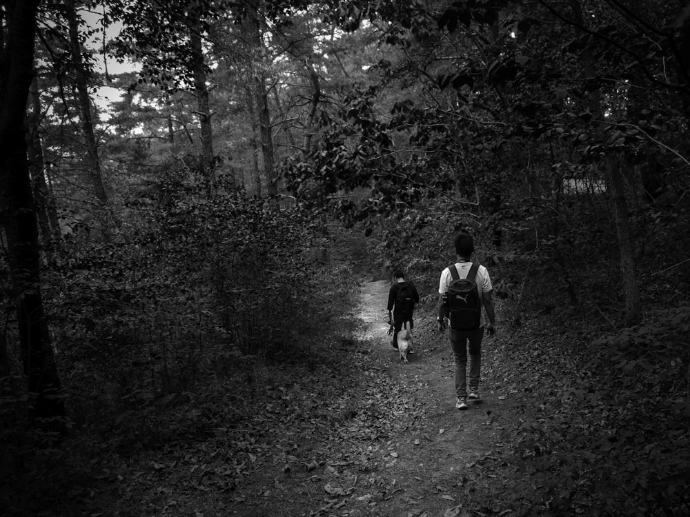 grayscale photo of 2 men walking on forest