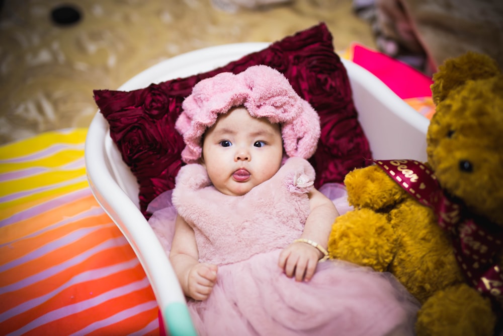 baby in pink dress lying on white and red striped bed