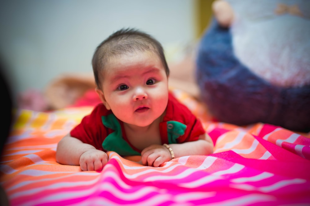 baby in green shirt lying on pink and white stripe bed