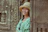 A smiling woman wearing a wide-brimmed hat stands gracefully in a beautifully tiled Moroccan riad courtyard.