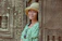 A smiling woman wearing a wide-brimmed hat stands gracefully in a beautifully tiled Moroccan riad courtyard.