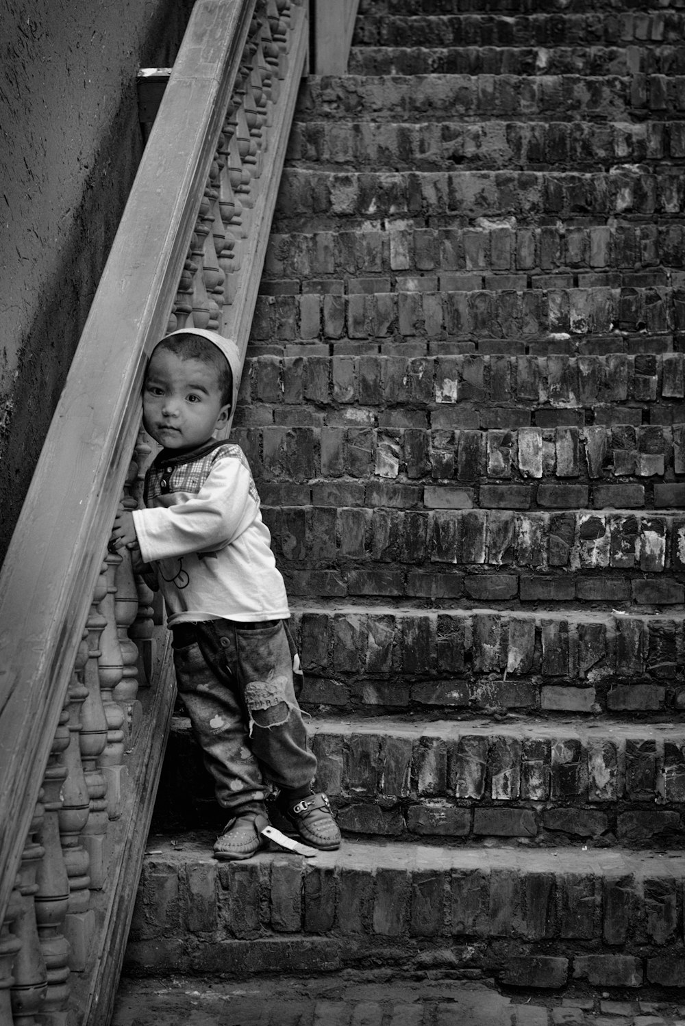 grayscale photo of child in long sleeve shirt and pants standing on stairs