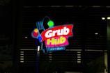 A brightly lit sign for Grub Hub Food Park, featuring the brand name in vibrant colors against a dark background. The sign includes graphic elements such as a fork and circles in various colors.