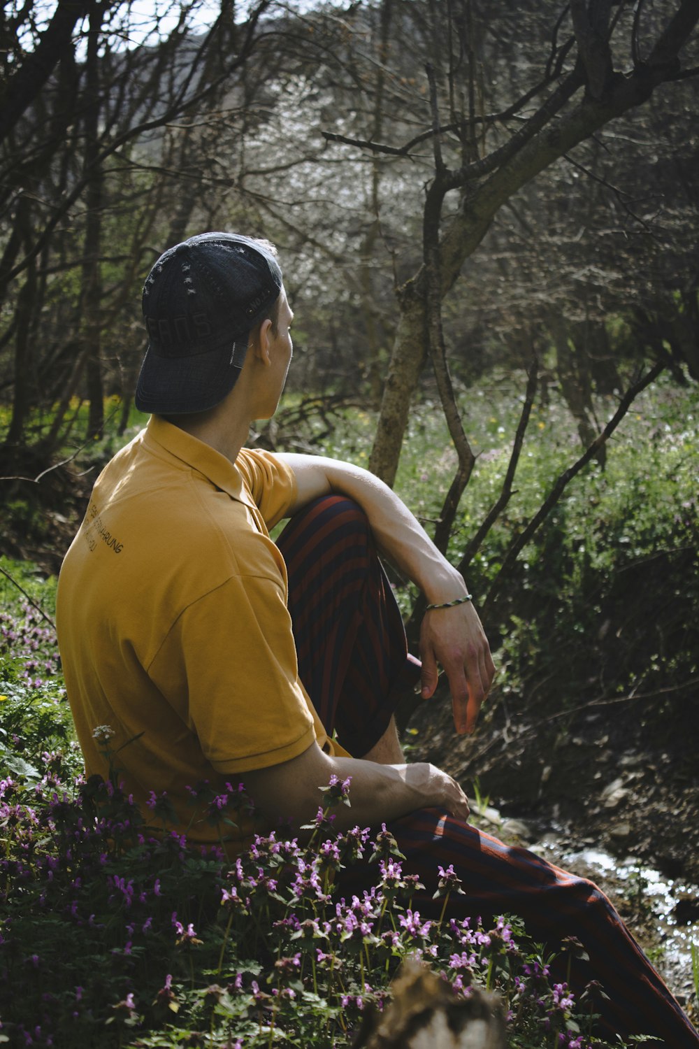 man in yellow polo shirt and black floral shorts sitting on ground surrounded by trees during