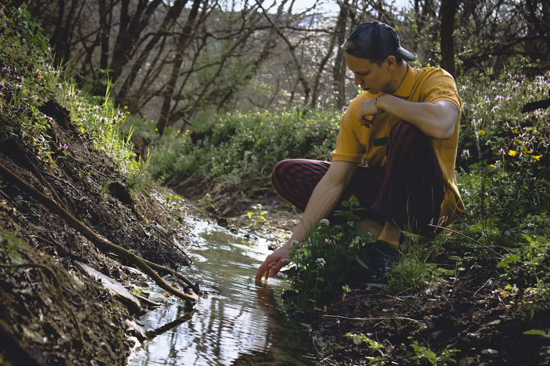 man in yellow shirt and black shorts sitting on rock near river during daytime