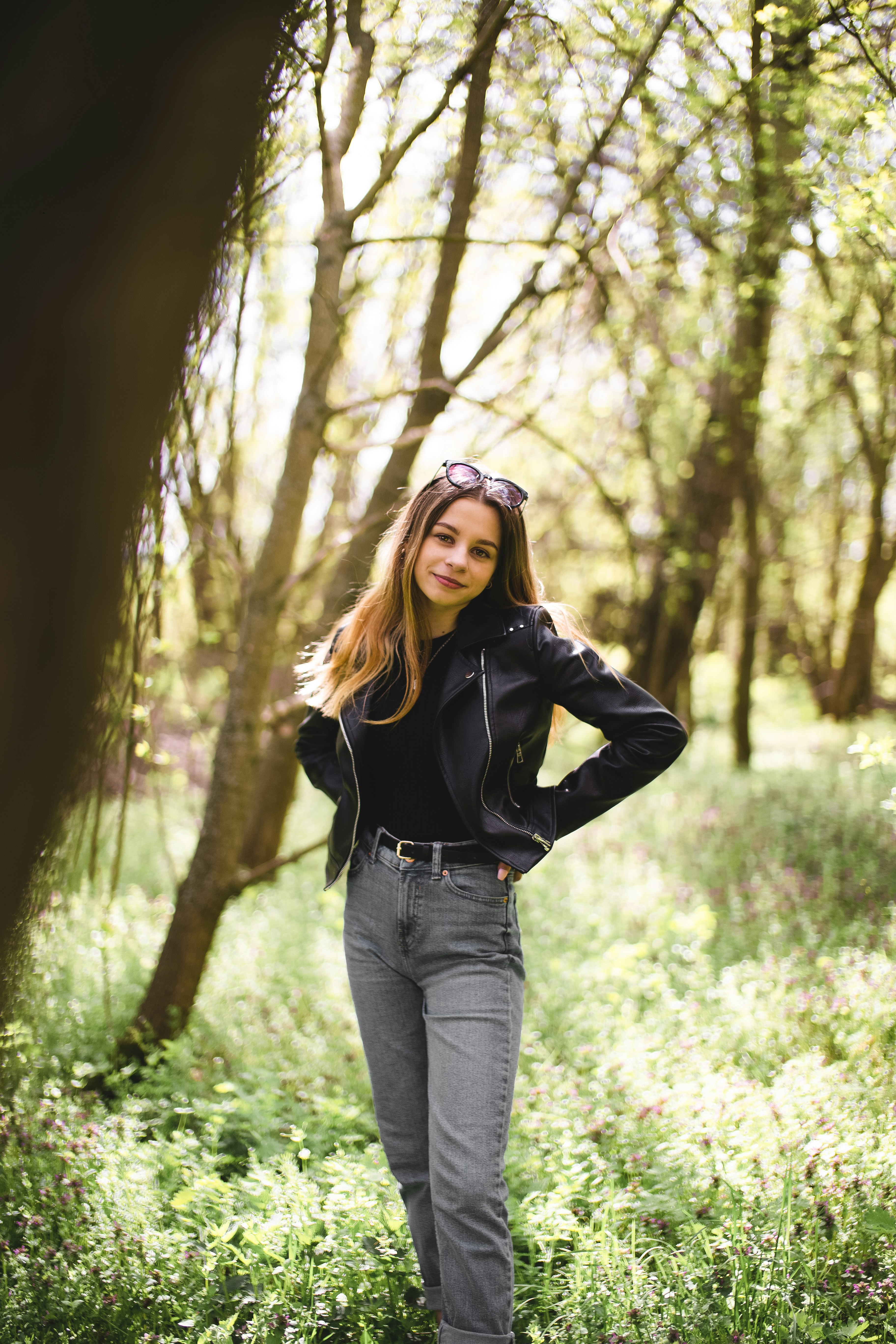 woman in black jacket and blue denim jeans standing in forest during daytime