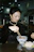 A smiling woman enjoying a vibrant bowl of Asian fusion noodles at a cozy dark-toned restaurant table.